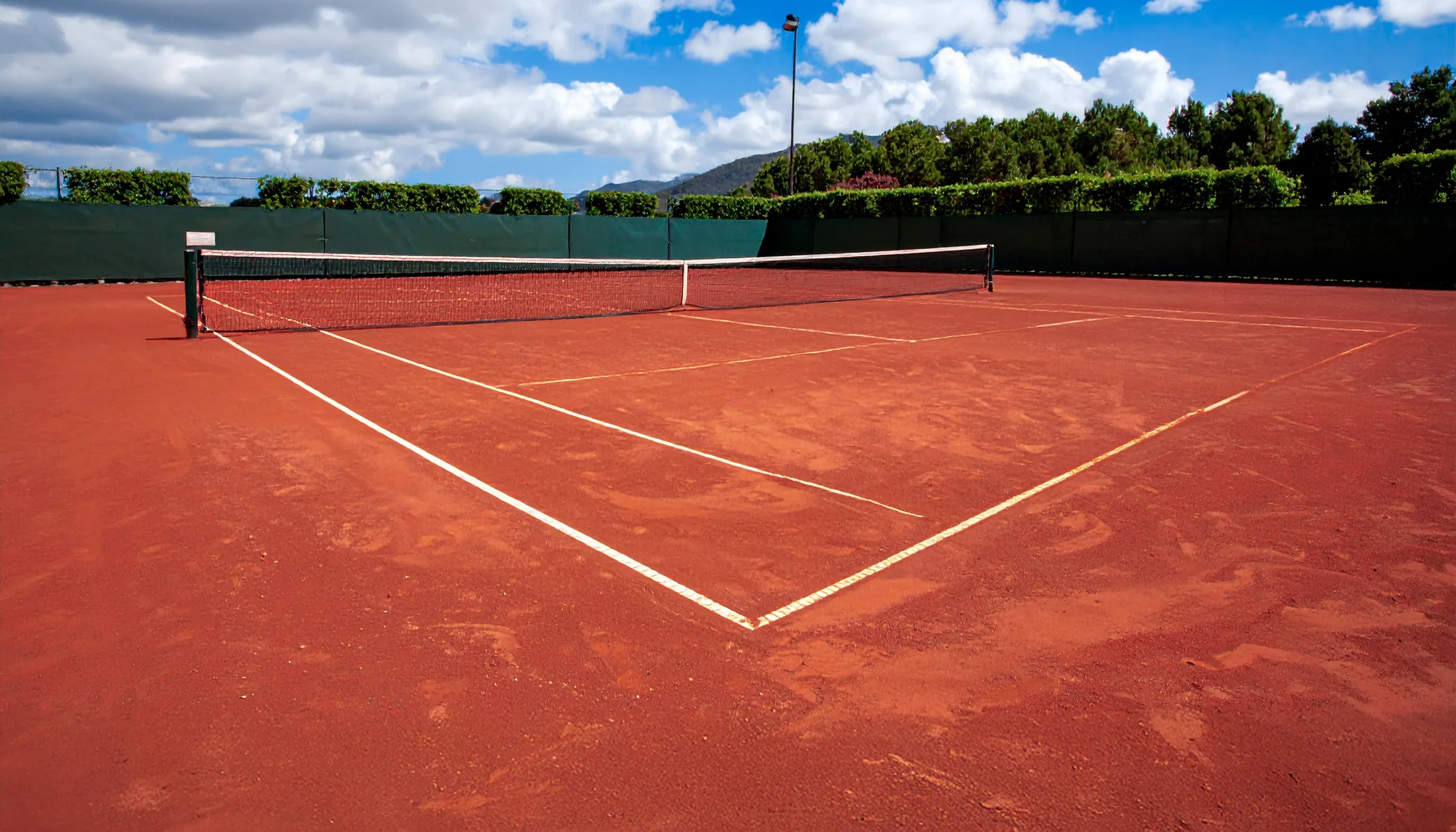 Red clay tennis court under a Mediterranean sky in Mallorca