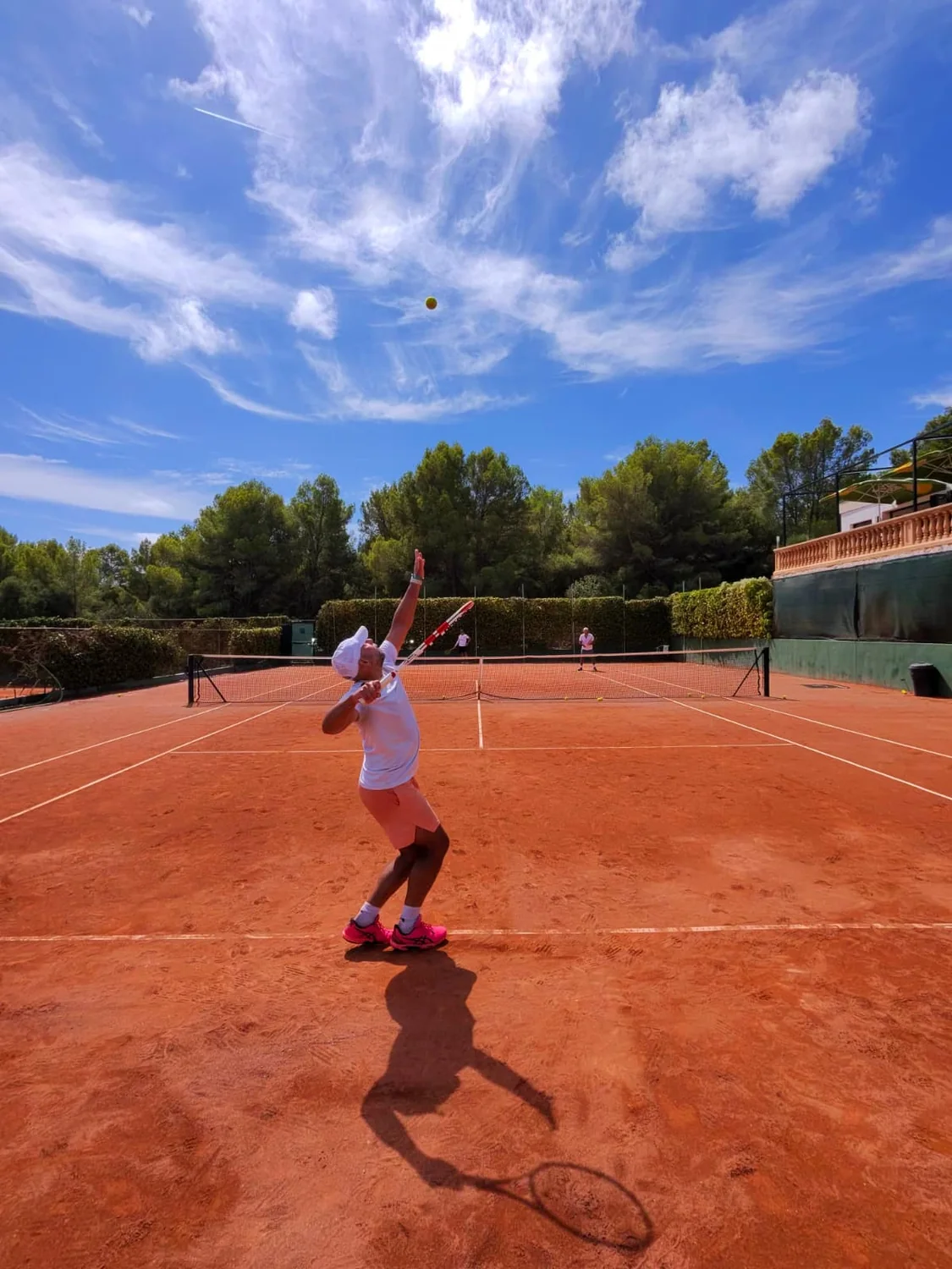 Tennis player serving on a red clay court in Mallorca